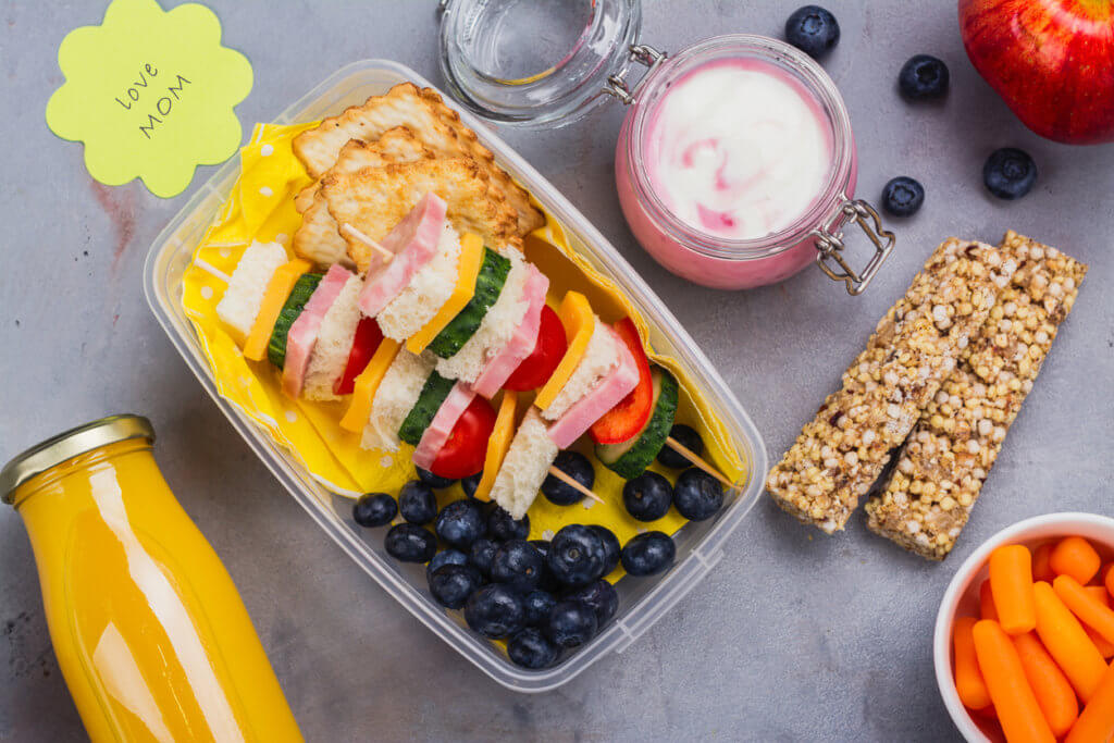 Healthy school lunch box with sandwich kabobs, yogurt, juice, fruits and berries
