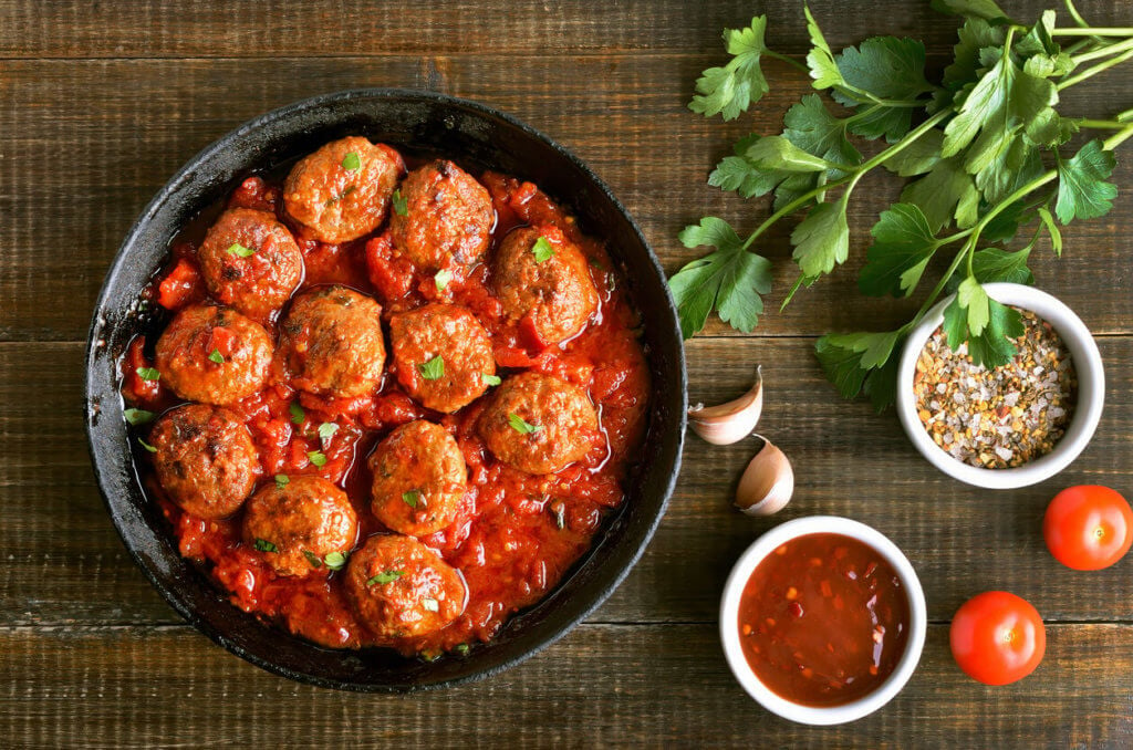 Meatballs in cast iron pan, fresh parsley and tomatoes