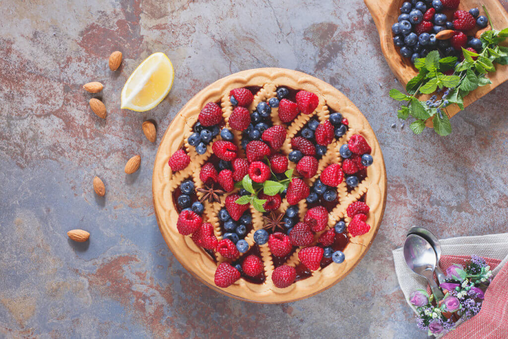 Whole homemade mixed berry lattice top pie on rustic table.