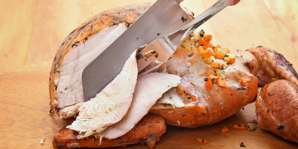 Hands cutting the roasted turkey into slices.