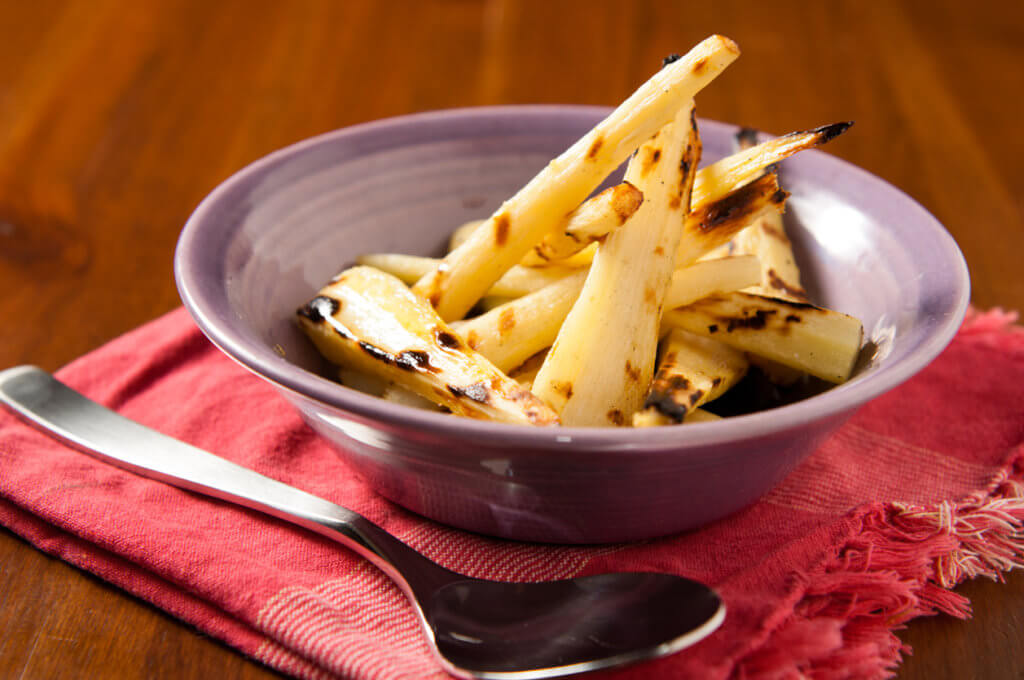 A bowl full of grilled parsnips drizzled with maple syrup.