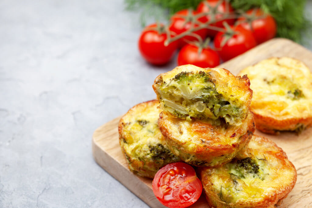 broccoli cheese bites (muffins), fresh tomatoes, fresh herbs on light concrete background. 