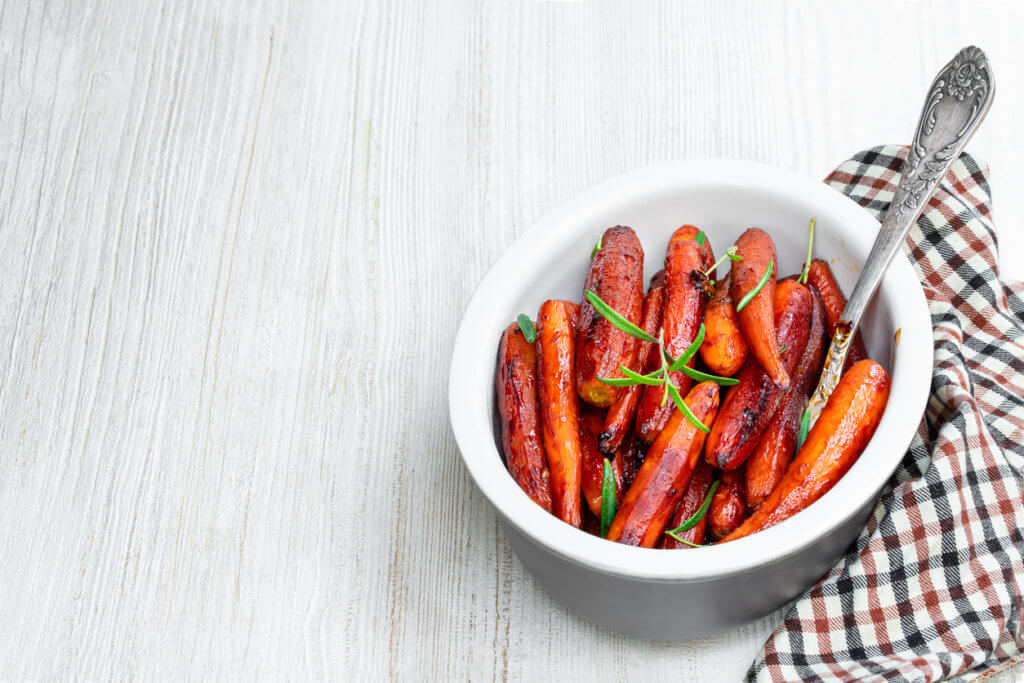 Grilled baby carrots with honey sauce and green herbs on white wooden table