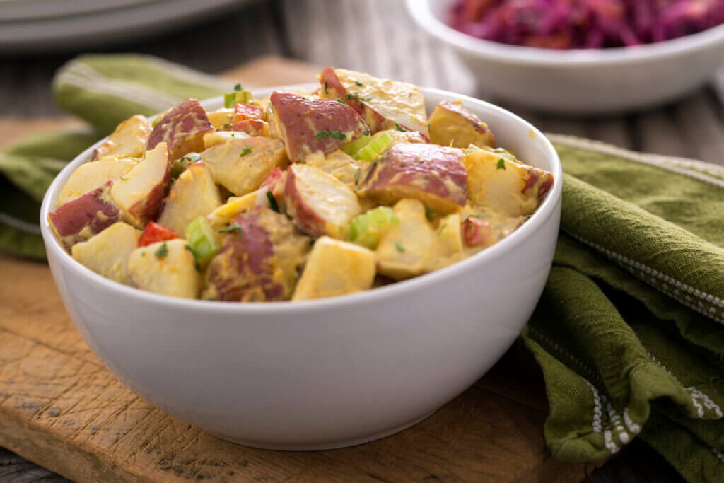 A bowl of potato salad and red cabbage coleslaw on rustic wood picnic table. 