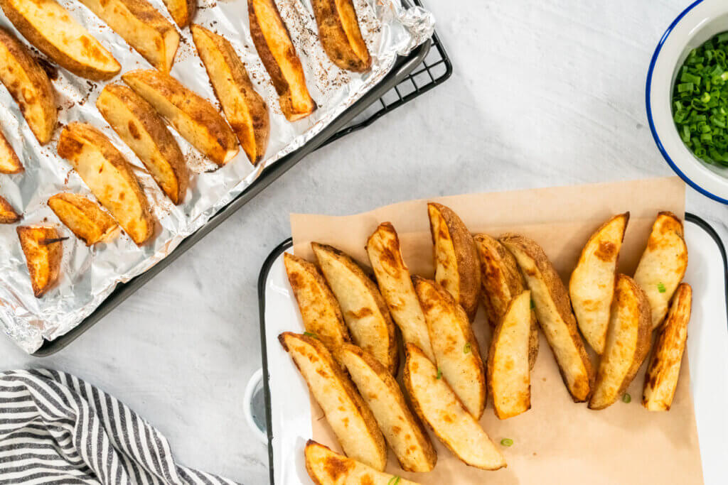 Freshly baked potato wedges with spices on a white serving tray.