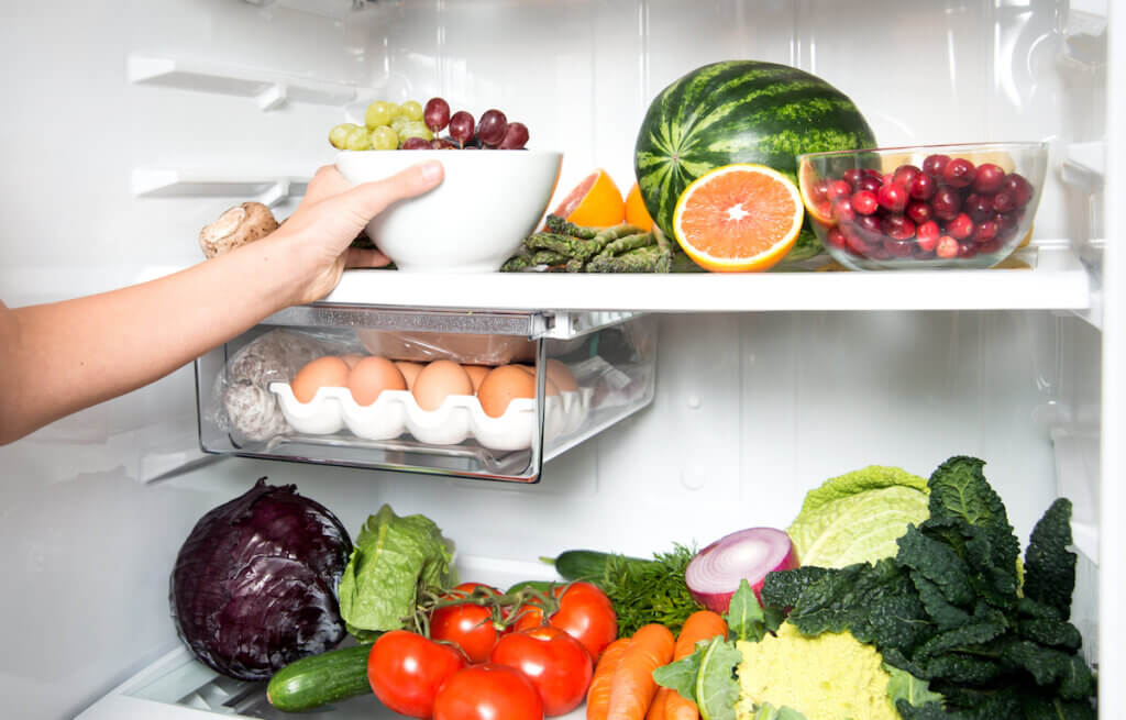 Hand Reaching for Green Apple in Refrigerator Full of Healthy Food Options