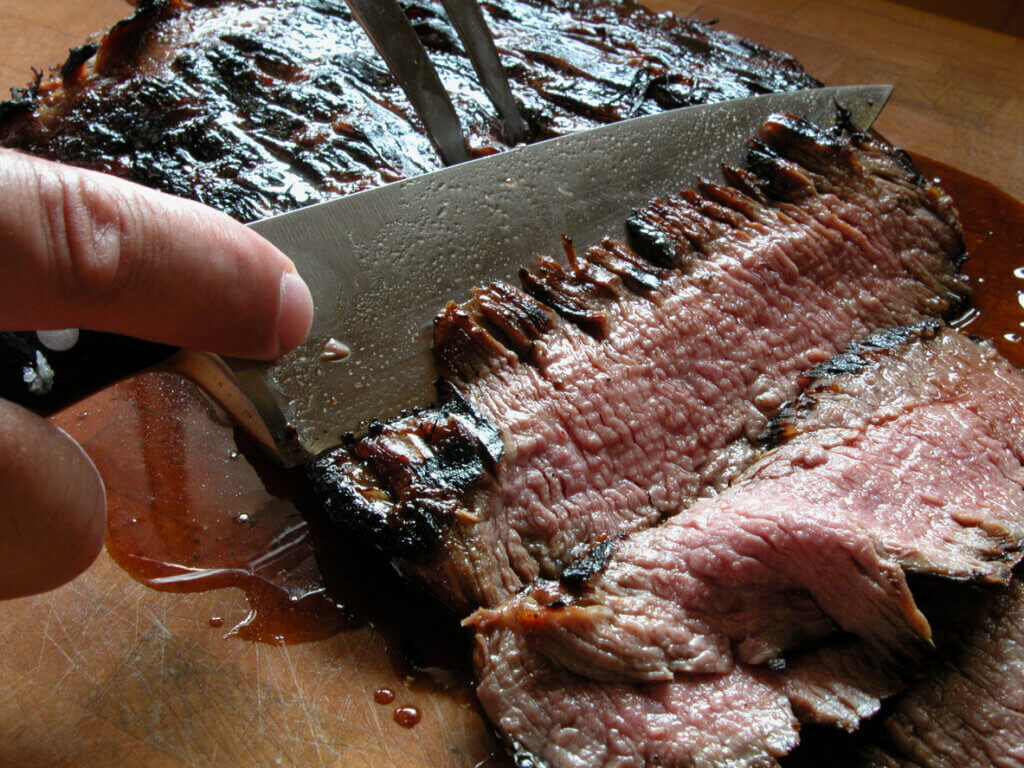 Close-up of a knife carving a piece of grilled flank stake