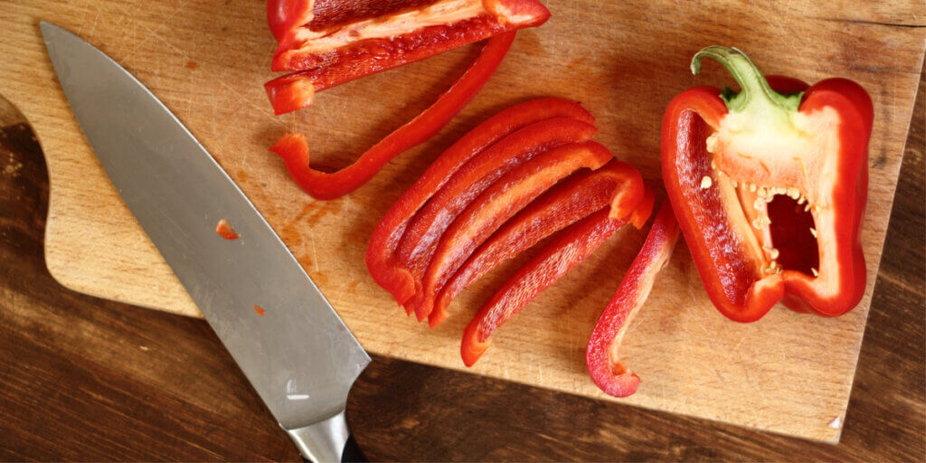 A half and strips of red bell pepper on a cutting board with a knife