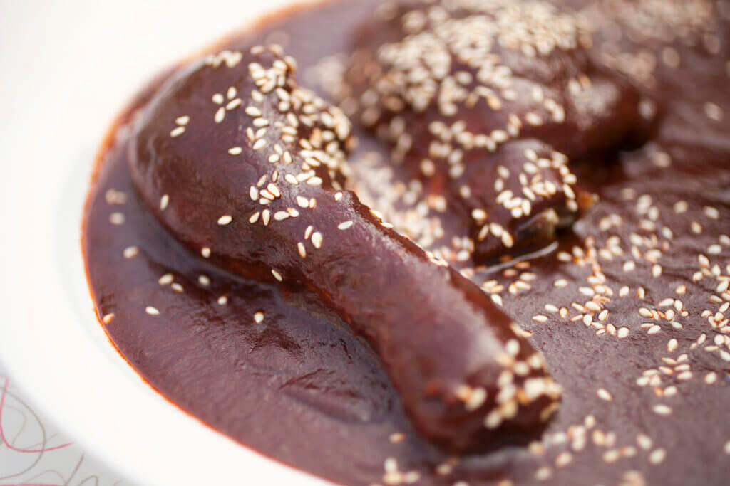 A chicken drumstick and thigh smothered in a rich mole sauce and sprinkled with sesame seeds.