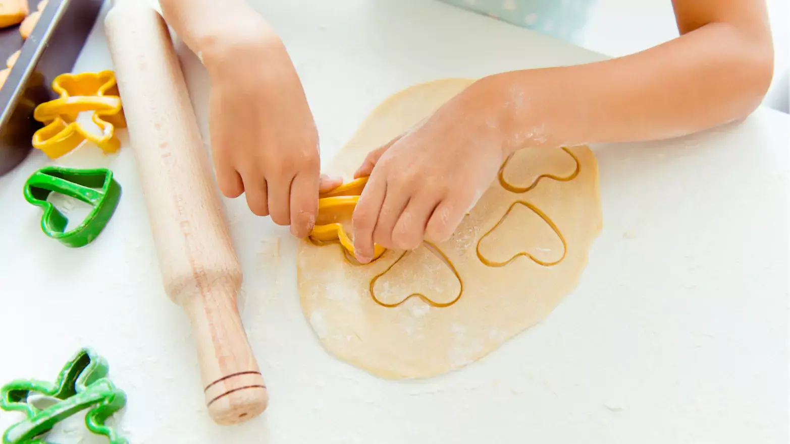 Young child using heart-shaped cookie cutter to cut sugar cookies