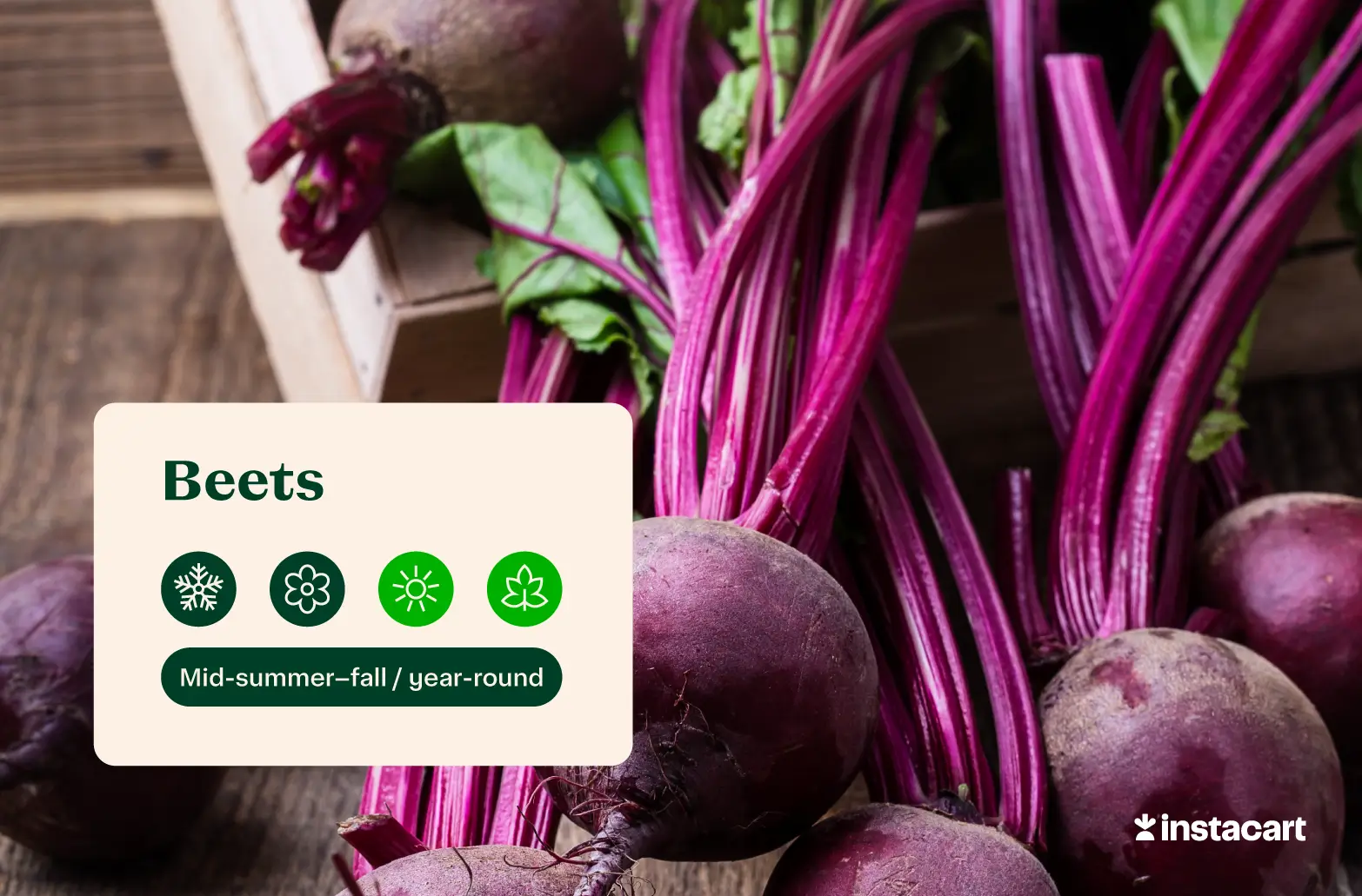 Dark red beets with red stems and green leaves on a wooden surface. 