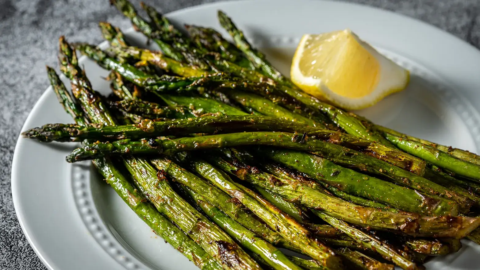 Plate of roasted asparagus with a slice of lemon. 