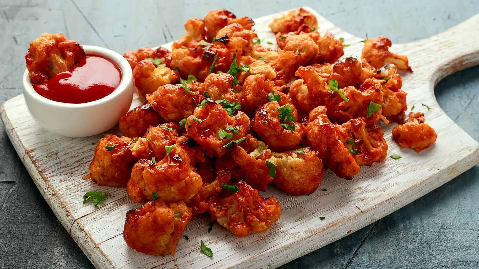 Cutting board with roasted buffalo cauliflower and dipping sauce.