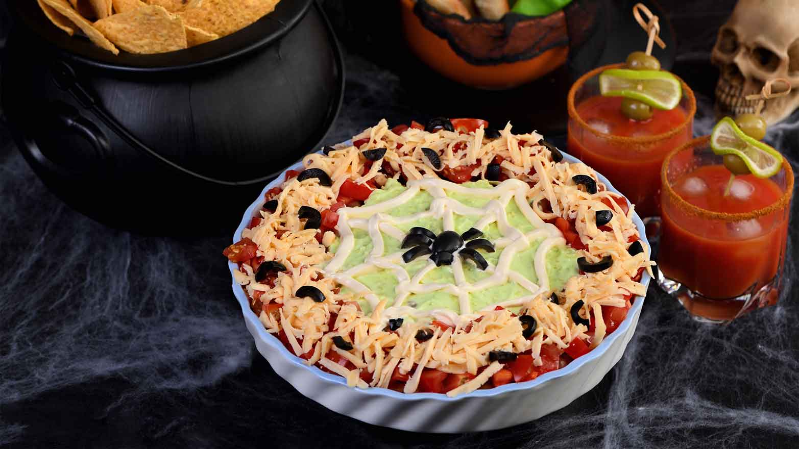 Seven layer dip with sour cream spider web on top with olive spider