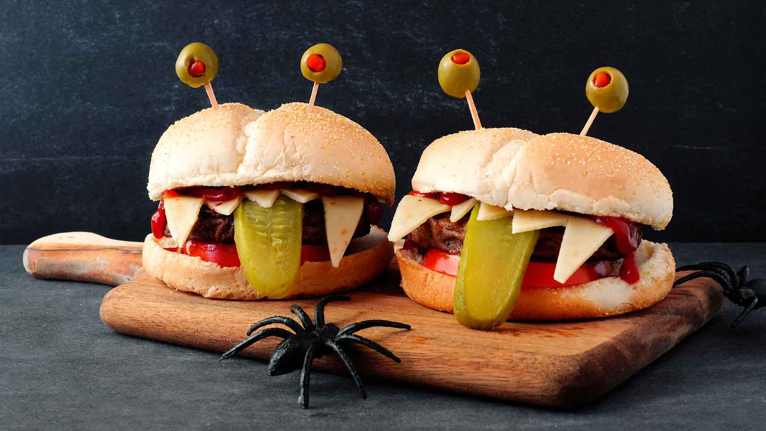 Monster burgers with black buns, olive eyes, and jagged cheese teeth