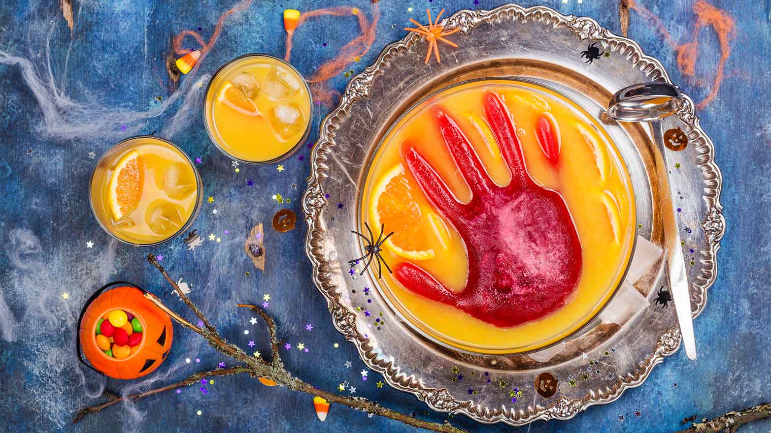 Ghoul's orange punch with bloody ice hand in a glass bowl on dark halloween background.