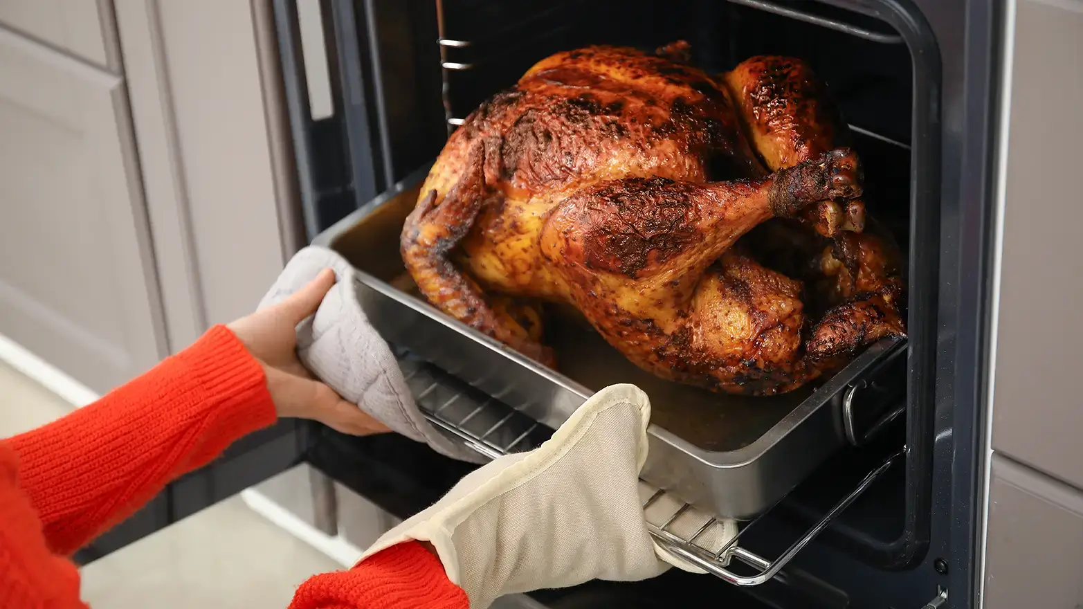 Stock image of person putting turkey in oven.