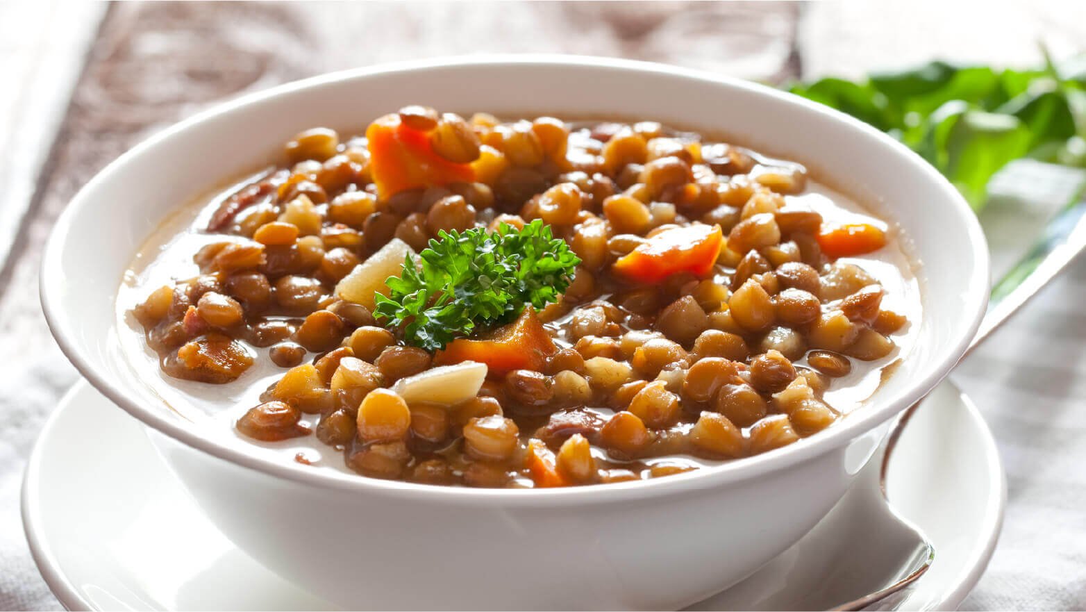 Large white bowl of lentil soup with a spoon to serve on Shabbat